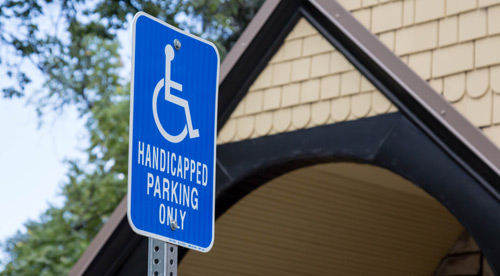 A blue sign that reads Handicapped Parking Only with the symbol of a person in a wheelchair stands outside a residential building