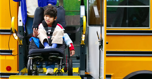 A young boy in a wheelchair rides a lift to get off his school bus