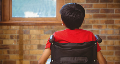 A Hispanic boy sits in a wheelchair facing away from the camera