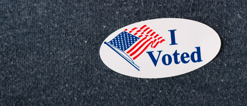 A close up of a blue sweatshirt with an oval shaped sticker featuring an American flag and the words I Voted