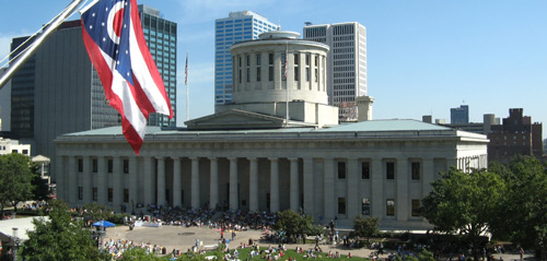 A photo of the Ohio Statehouse with the Ohio flag in the foreground