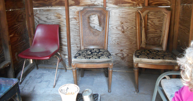 Three chairs in a wooden hut the residents of Simmons Adult Care used for smoking. The backs of two of the chairs are broken.