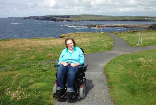 Susan Koller poses in her wheelchair in front of a beautiful blue lake