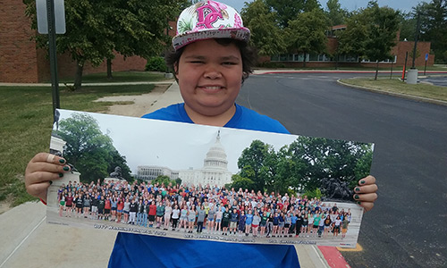 Tasia, a middle-school girl wearing a floral D.C. baseball hat, holds a picture of her class standing in front of the U.S. Capitol Building.