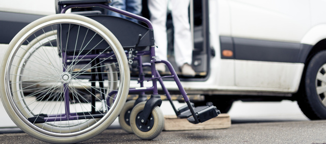 Wheelchair in front of van with door open, with the legs of two people in the van