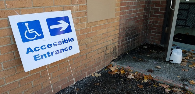 A sign that reads Accessible Entrance and points to an open door is propped on a wall outside a polling location