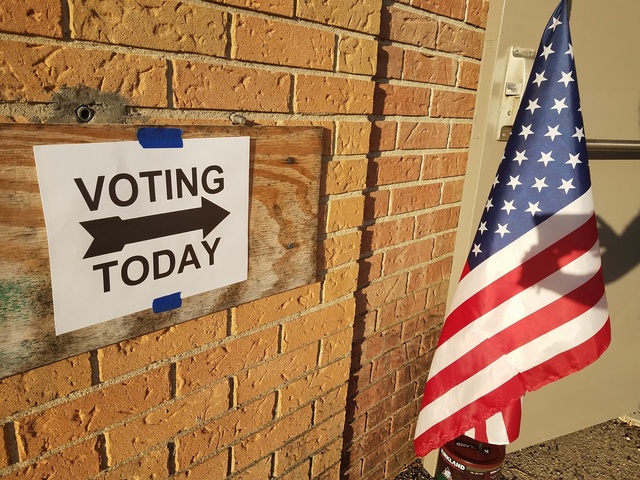 A Voting Today sign with an arrow points to an open door next to an American flag