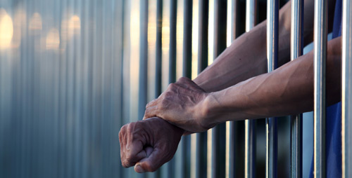 White_man_arms_prison_bars_cropped