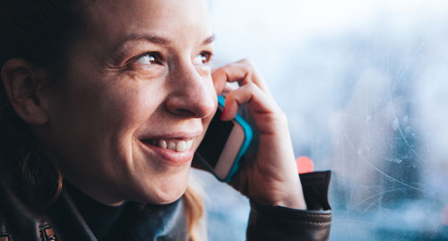 A young white woman smiles as she talks on her phone while riding the bus