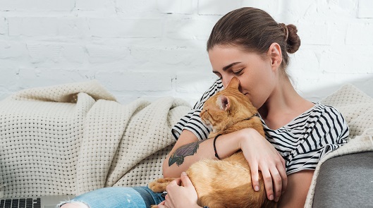 A young woman cuddles on a couch with an orange tabby cat