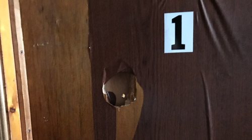 Picture shows a hole in a wall with peeling wall coverings and exposed wood in the door frame
