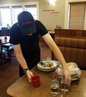Zach Ricker takes dishes off of a table so they can be washed at the Bob Evans in Bellefontaine, where he works